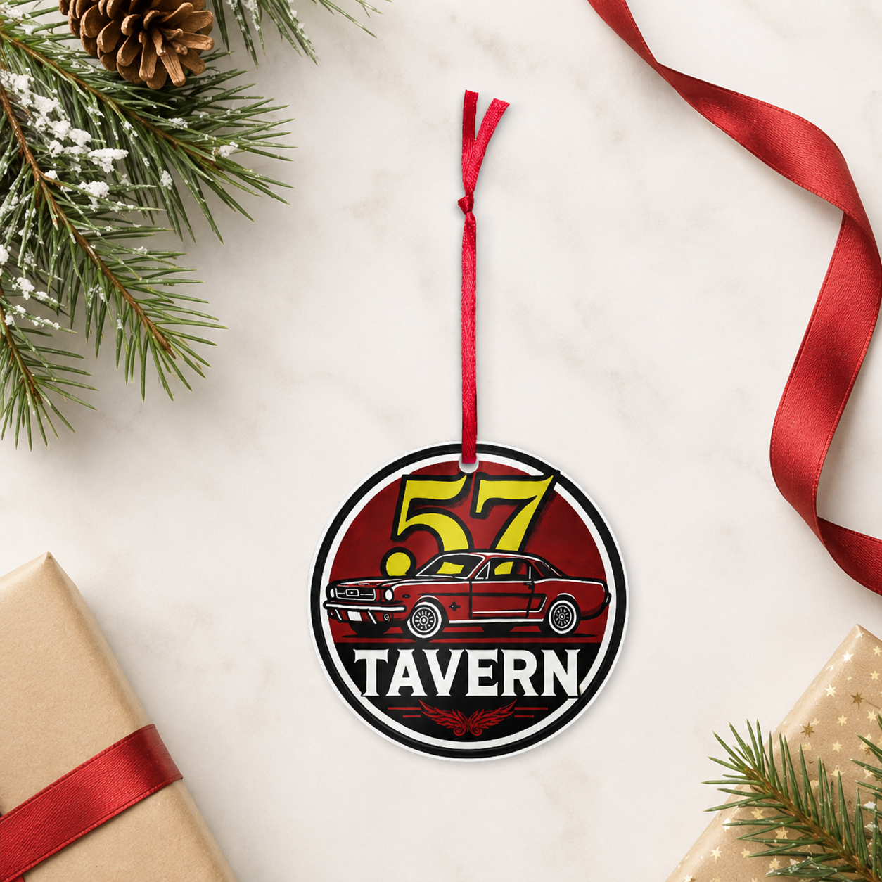 A round hanging ornament with a red ribbon loop, featuring a red car and the words “57 TAVERN,” styled on a light marble surface with pine branches, a pinecone, wrapped gifts, and a red ribbon.