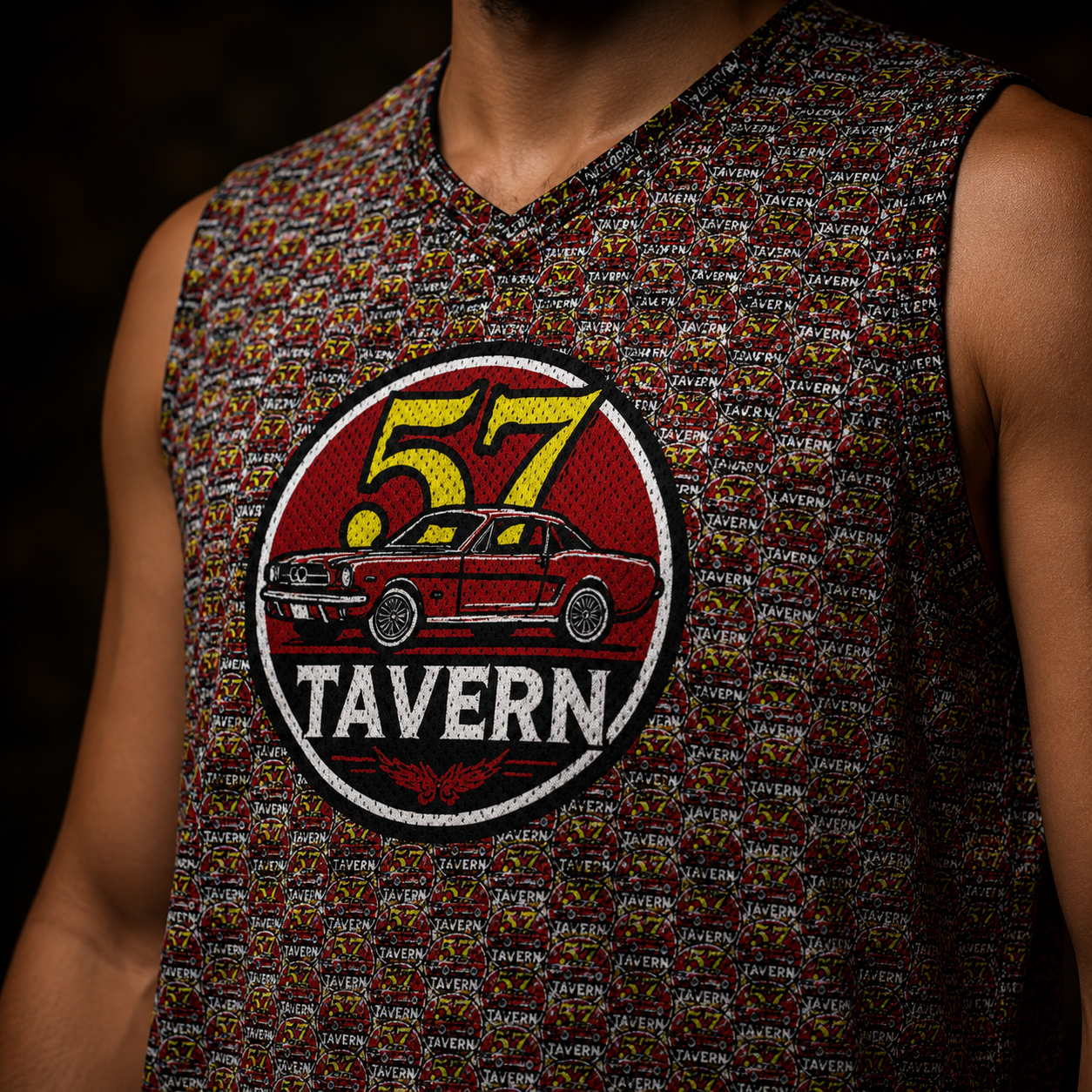 Close-up of a sleeveless V-neck tank top worn by a person, featuring a dense multicolor pattern and a large circular chest graphic with a red car, yellow '57', and the words '57 TAVERN'.