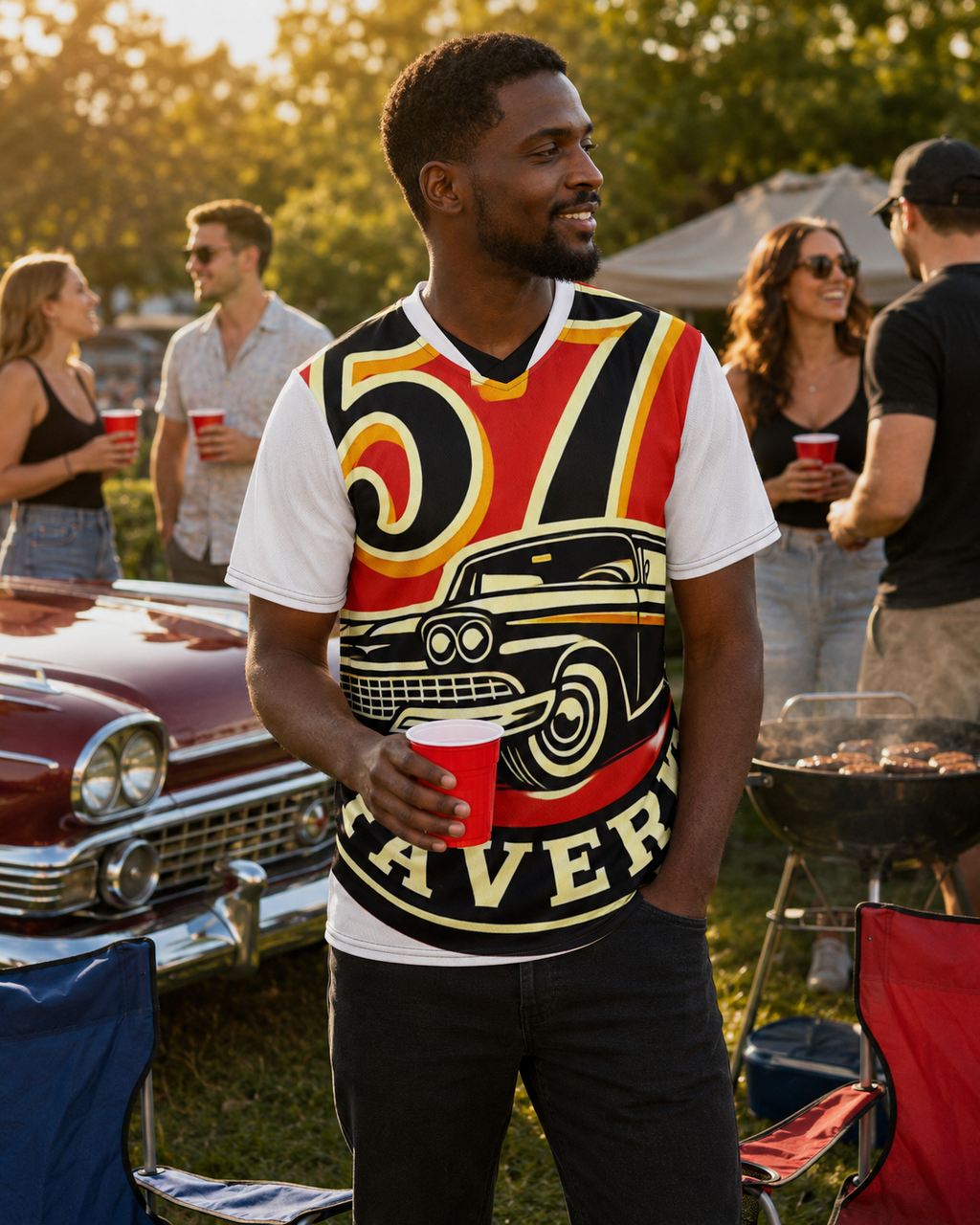 A man standing at an outdoor barbecue gathering wearing a graphic t-shirt with a vintage car design and the word 'Cruiser'.