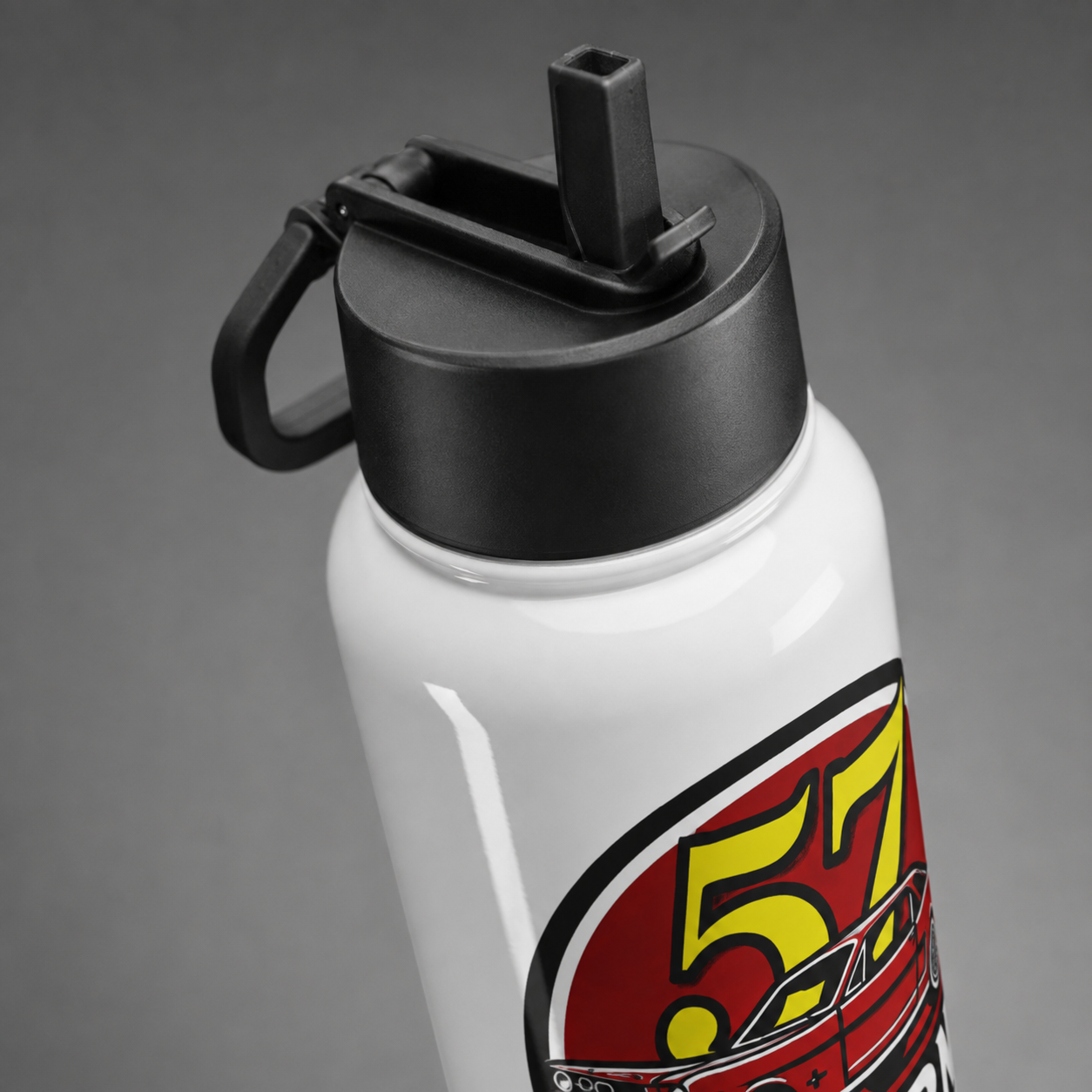 A close-up of a white insulated water bottle with a black flip-straw lid and a red, yellow, and black racing-style graphic on the lower portion, shown on a gray studio background.