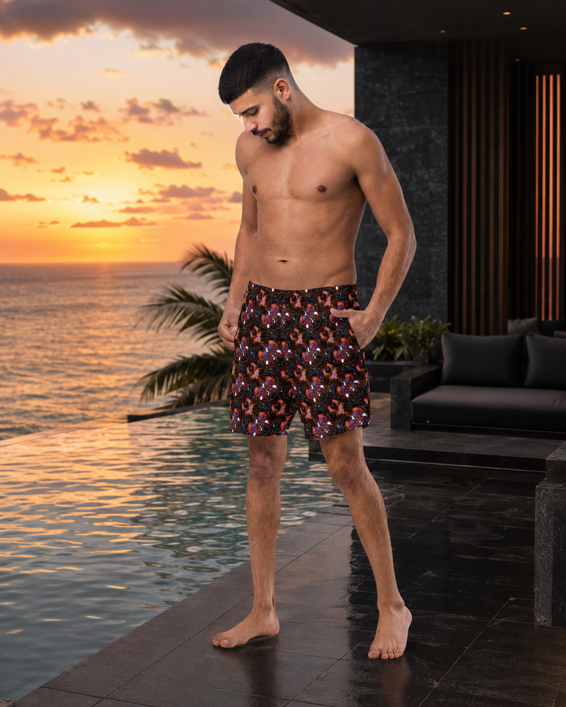 A shirtless man wearing patterned swim trunks stands by an infinity pool at sunset, with ocean water, palm leaves, and a modern outdoor lounge area in the background.