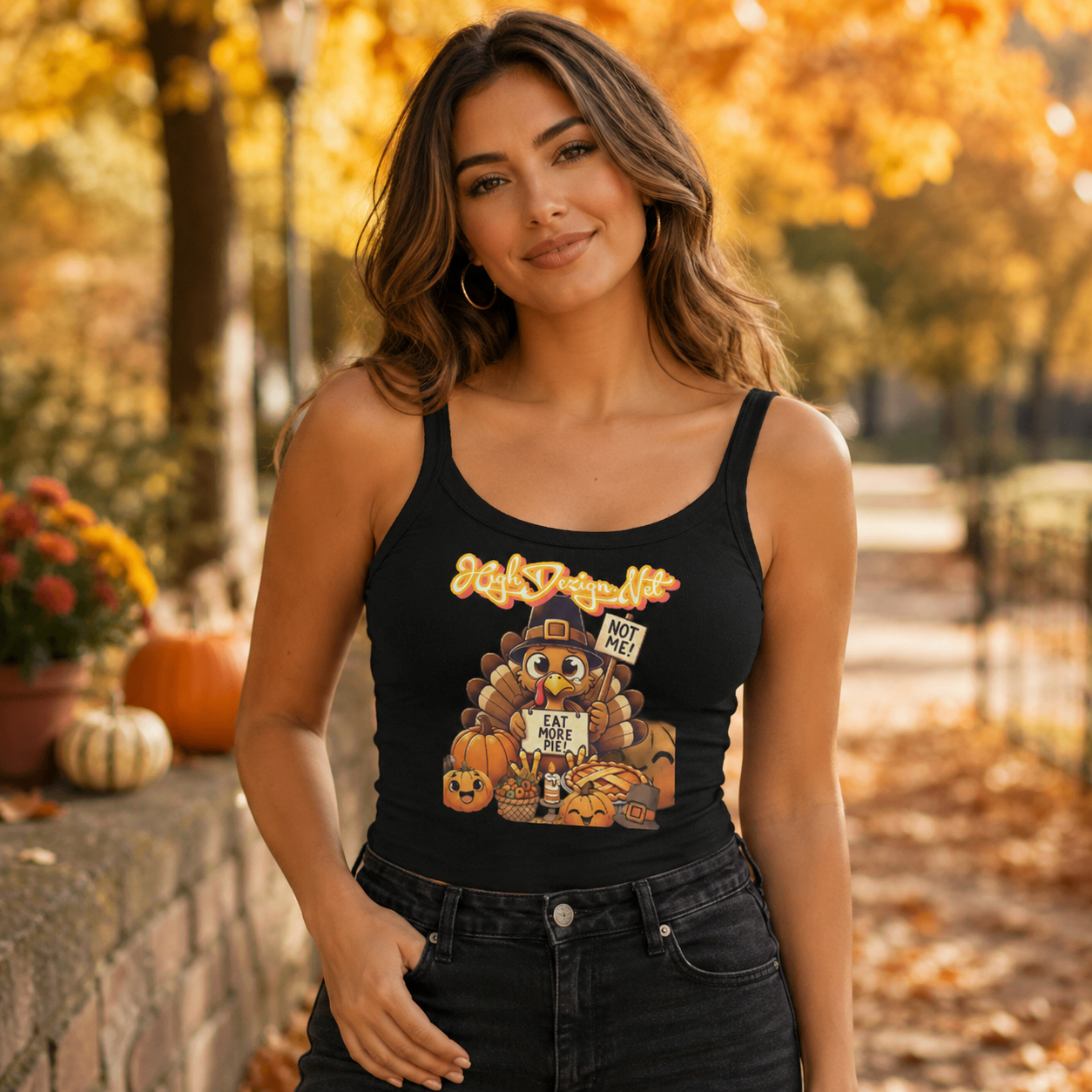 A woman wearing a black tank top with a colorful Thanksgiving turkey graphic and the text 'Happy Thanksgiving' and 'Have a Great Week' stands outdoors in a fall park setting with pumpkins and autumn trees.