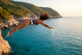 Person diving into the ocean from a cliff with a scenic background