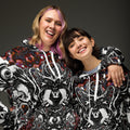 Two people wearing matching black and white patterned hoodies against a dark background