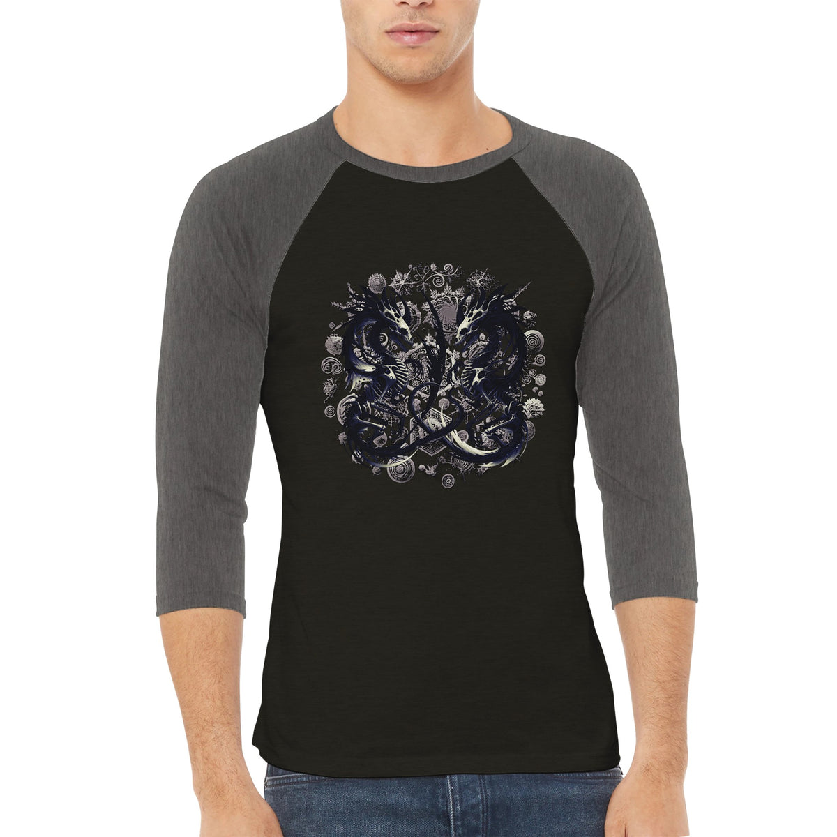 A man wearing a 3/4-sleeve raglan baseball t-shirt with a dark gray body and sleeves, featuring a detailed circular graphic print on the chest with skulls, coins, and a central figure.