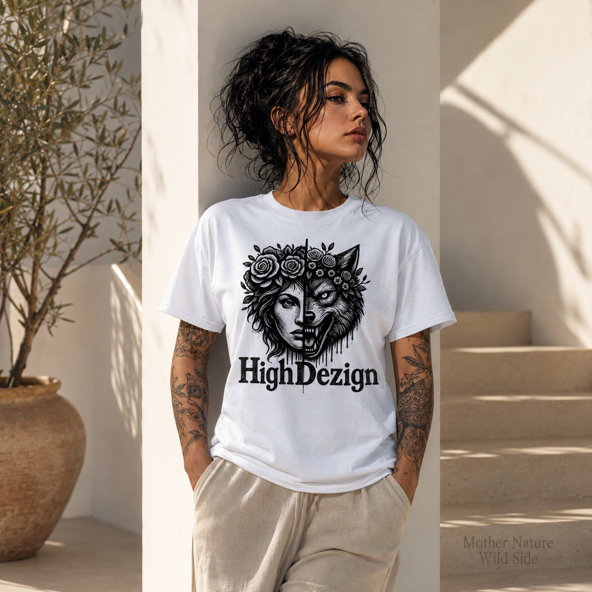 A woman wearing a white graphic t-shirt with a black wolf and rose design and the text 'HighDezign', paired with beige pants, standing in a sunlit architectural setting.