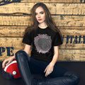 A person wearing a black crew neck t-shirt with a graphic design, sitting against a wooden backdrop.