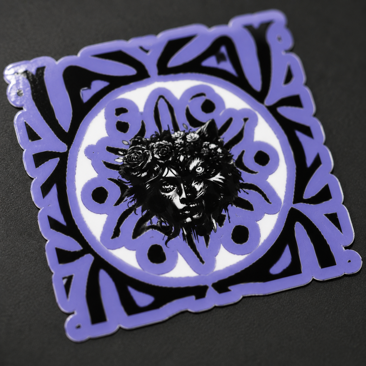 A square decorative sticker or patch with a purple border and a black-and-white central illustration of a face surrounded by flowers, shown on a dark background.