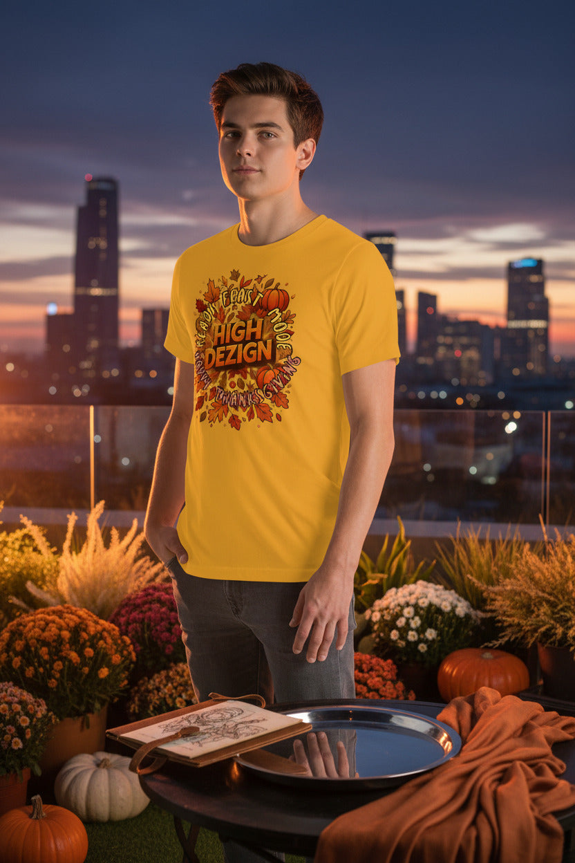 A young man stands on a rooftop terrace at dusk wearing a bright yellow graphic t-shirt with a fall-themed 'High Design' graphic. The background features a city skyline at sunset, with potted mums, pumpkins, and a table with an open book and a silver tray in the foreground.