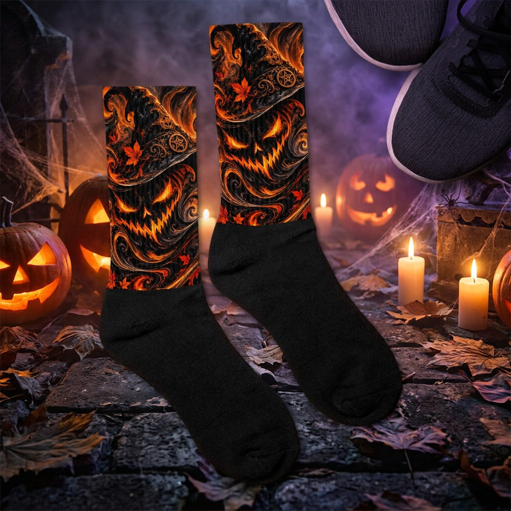 A pair of crew socks laid flat on a wooden floor, with one sock showing a black-on-brown repeating monogram pattern and the other showing the solid black reverse side. Part of a gray sneaker is visible in the top-right corner..