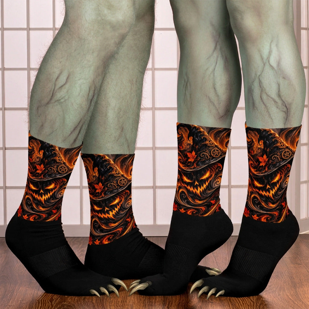 Three pairs of black crew socks with a fiery orange and yellow jack-o'-lantern pattern, shown on human legs against a tiled wall and wooden floor..