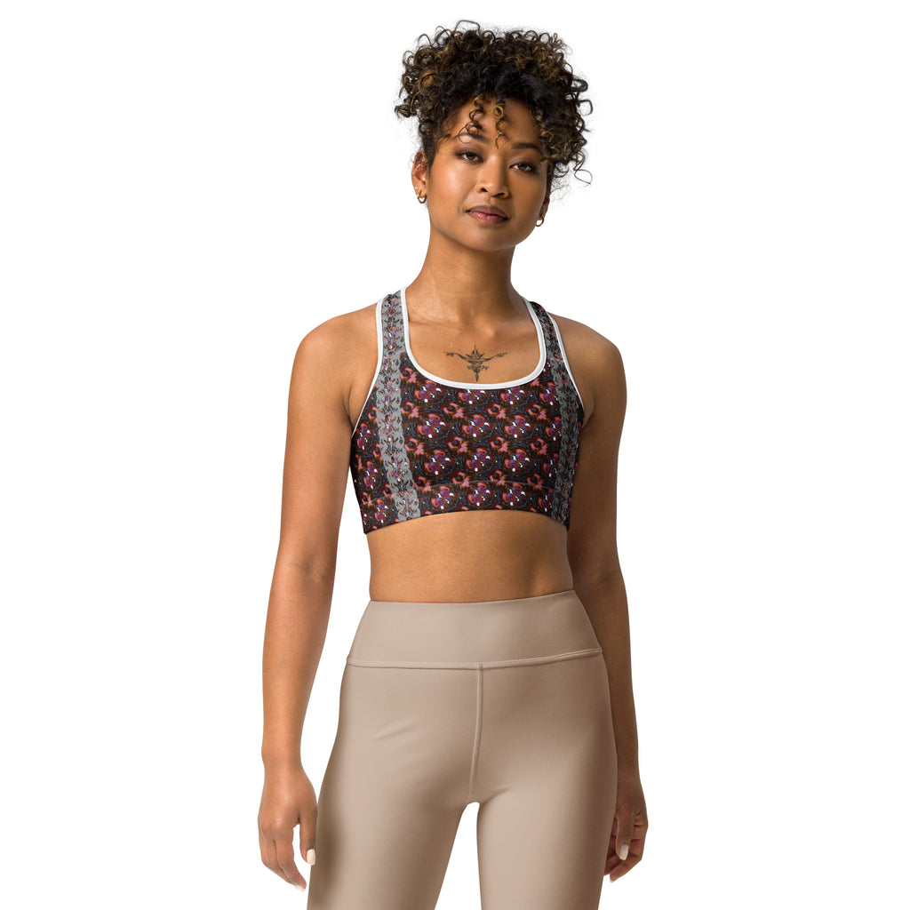 A woman modeling a sports bra with a dark floral pattern and gray patterned straps, paired with beige leggings, against a solid white background.
