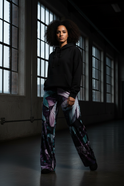 Person wearing a black hoodie and colorful pants in a dimly lit room with large windows.